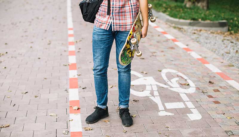 guy carrying skateboard in bike path