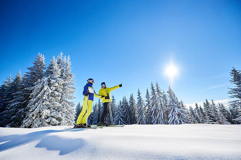 two skiers look out on snowy slope